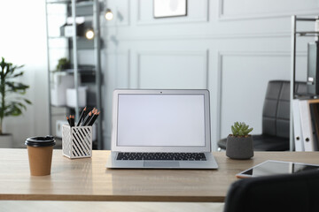 Stylish workplace with laptop, stationery, coffee and floral decor on wooden table in office
