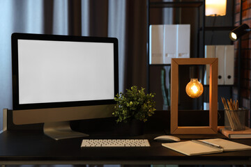 Computer, houseplant, lamp and stationery on black table indoors