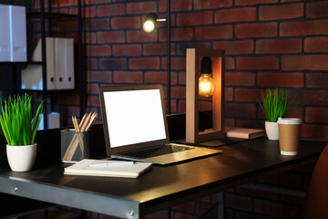 Laptop, takeaway paper cup, houseplants and stationery on black table near brick wall