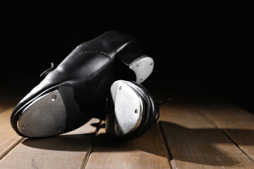 Pair of tap shoes on wooden floor against black background, closeup. Tap dance