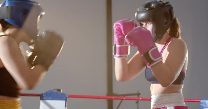 Stepping into gym ring, two women boxers donning headgear and gloves, sparring jabs to test timing