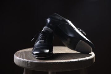 Pair of shoes for tap dance on wooden stool against black background, closeup