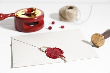Envelope with wax seal and stamp on white wooden table, closeup