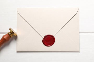 Envelope with wax seal and stamp on white wooden table, top view