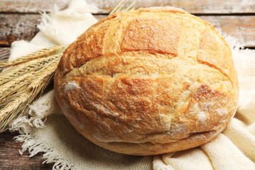 Loaf of fresh bread and wheat spikes on wooden table, closeup
