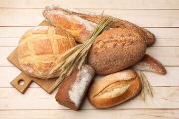 Different types of bread and wheat spikes on wooden table, flat lay