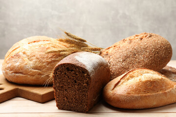 Different types of bread and wheat spikes on wooden table, closeup