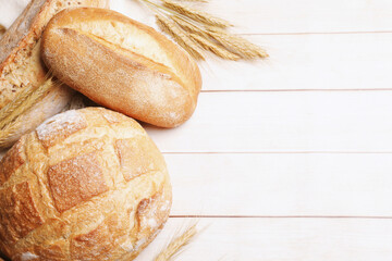 Different types of bread and wheat spikes on wooden table, flat lay. Space for text