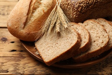 Different types of bread and wheat spikes on wooden table, closeup