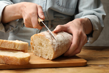 Woman cutting fresh bread at wooden table, closeup