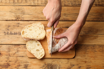 Woman cutting fresh bread at wooden table, top view