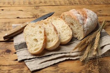 Fresh bread, wheat spikes and knife on wooden table, closeup