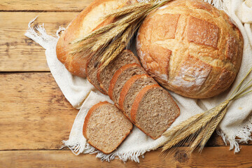 Different types of bread and wheat spikes on wooden table, flat lay. Space for text