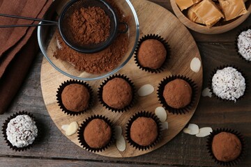 Delicious homemade candies with cocoa powder and coconut flakes on wooden table, flat lay