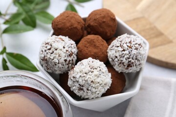 Delicious homemade candies with cocoa powder, coconut flakes and tea on white table, closeup