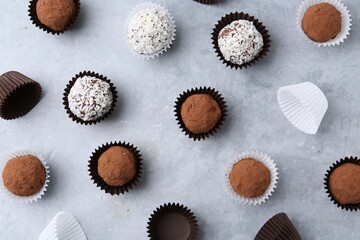 Delicious homemade candies with cocoa powder and coconut flakes on light grey table, flat lay