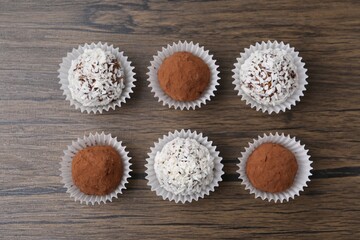Delicious homemade candies with cocoa powder and coconut flakes on wooden table, flat lay