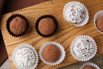 Delicious homemade candies with cocoa powder and coconut flakes on table, top view