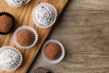 Delicious homemade candies with cocoa powder and coconut flakes on wooden table, flat lay. Space...