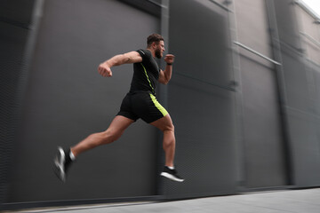 Man in sportswear running near building outdoors, motion blur effect. Low angle view