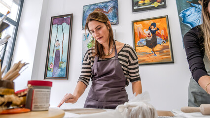 A shot of a middle-aged woman artist shaping clay with sculpting tools at a table in an art studio,...