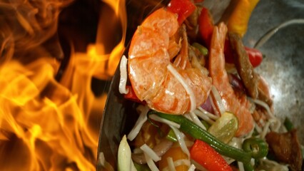 Closeup of chef throwing asian vegetable with meat mix from wok pan in fire. Fresh asian food...