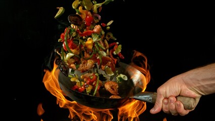 Closeup of chef throwing asian vegetable with meat mix from wok pan in fire. Fresh asian food...