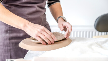In an art studio with an environment adorned with artistic paintings in the background, a beautiful middle-aged woman artist is shaping clay with her hands at a table