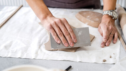 In an art studio with an environment adorned with artistic paintings in the background, a beautiful middle-aged woman artist is shaping clay with her hands at a table