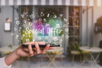Moblie shopping device app, hand holding smartphone with word writing Special Offer and icons app hologram symbols concept, shop front background