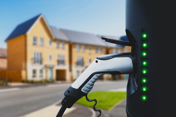 Electric home car charging station with the power cable supply plugged in with house in the...
