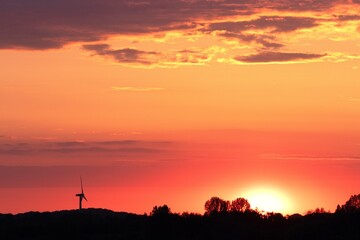 Windkraftanlage bei Sonnenuntergang mit rotem Aendhimmel.