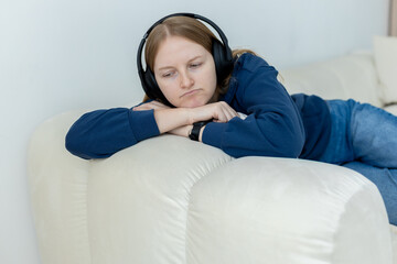 Sad woman listening to music wearing headphones lying on the sofa at home