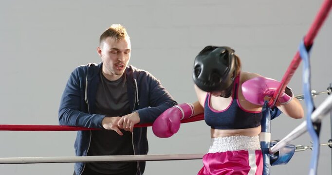Stepping into ring corner, female boxer adjusting pink gloves while absorbing coach instructions