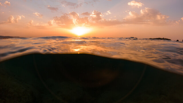 Underwater part and sunset skylight splitted by waterline, underwater bubbles. Beautiful clouds and bright sun over sea water, Real image very suitable for backgrounds in Mediterranean sea, undersea.