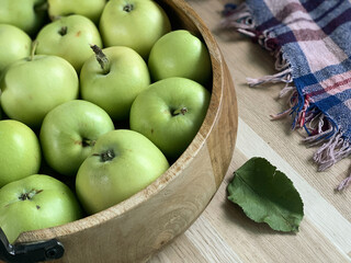 side view of a wooden bowl with green apples on a wooden table