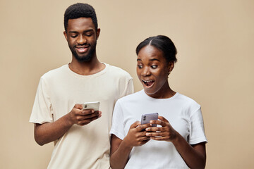 Happy young African couple sharing exciting news on smartphones, expressing joy and engagement in a...