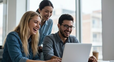 Three diverse colleagues collaborating and laughing at a laptop during a meeting, showcasing teamwork and positive workplace culture