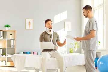 Male young doctor traumatologist examining man patient wearing neck brace with broken arm in...