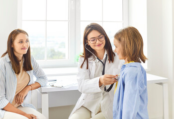Friendly female pediatrician using stethoscope, checking heartbeat of little child during medical...