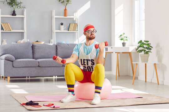 Funny man exercises with dumbbells at home during his fitness workout. He stays active by doing strength training and improving his fitness, showing dedication to sports and home gym routines.