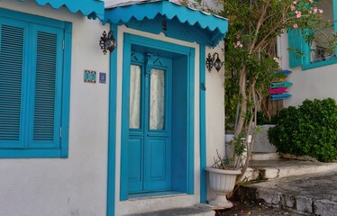 Fototapeta premium A white building with striking blue doors and window frames evokes a Mediterranean atmosphere. Lush greenery adds a touch of nature to the scene in old Marmaris - Mugla - Turkey