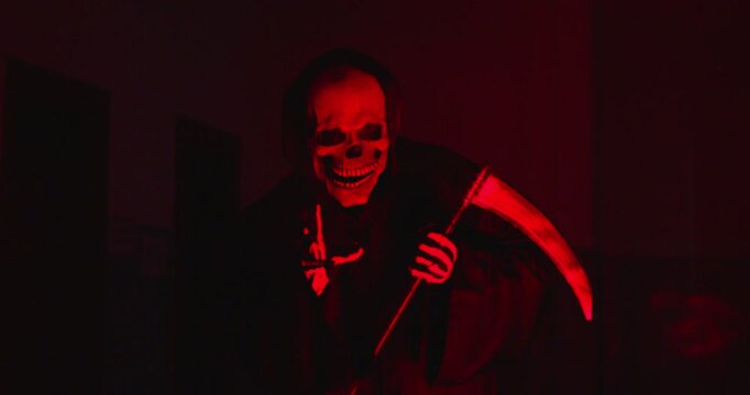 Horrible and awful grim reaper portrait illuminated by red light at a Halloween party. This demon like figure, holding a scythe, creates a nightmarish scene filled with horror and fear.