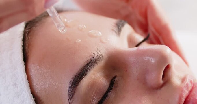 Cosmetologist is seen carefully applying moisturizing serum to clients face in spa setting. Close up of face of relaxed woman having serum gently rubbed into her skin for hydration and rejuvenation.