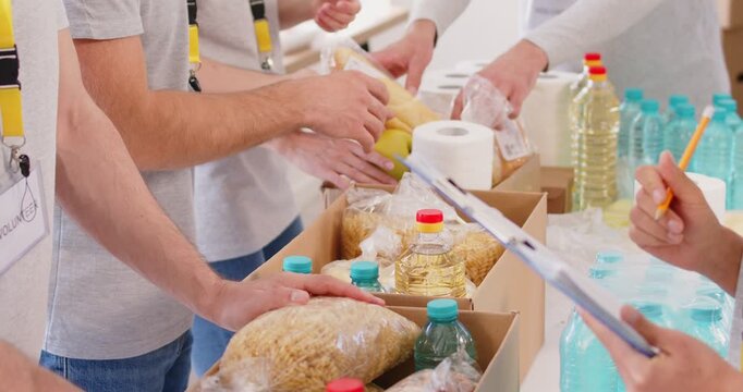 Slow motion video of volunteers packing food grocery in donations box for charity food drive. People volunteering in food bank working in charitable foundation.