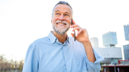 Senior man smiling while talking on smartphone outdoors