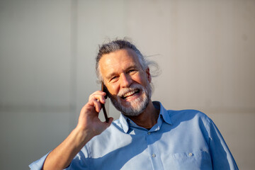 Cheerful elderly man laughing during phone call outdoors