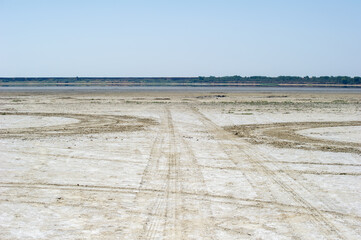 Tire tracks stretch across a dry, barren landscape under a clear blue sky, hinting at human...