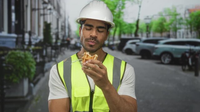 Man eating golden waffle on busy urban street wearing yellow vest and engineer hardhat; satisfaction.