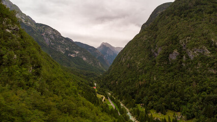 Naklejka premium Majestic Mountain Valley with Lush Forests and Rugged Peaks Under a Cloudy Sky